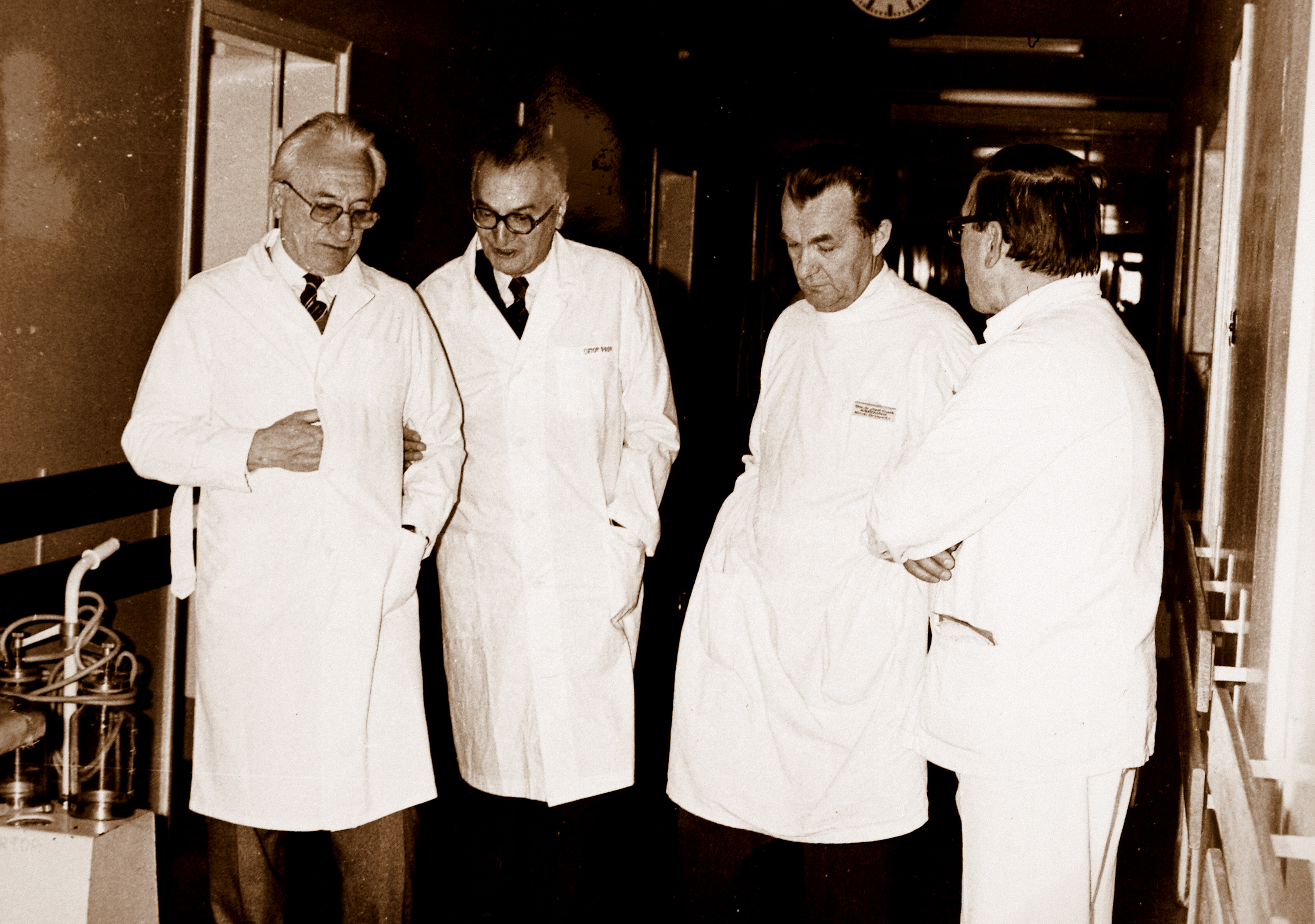 Czterech mężczyzn w kitlach rozmawiających na korytarzu